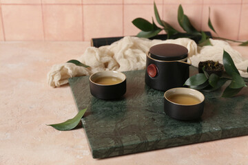 Cups of hot tea and teapot on light background