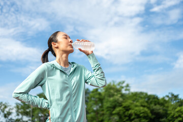 Happy slim asian woman drinking water after workout exercising on running track at sport stadium. Young beautiful asian drinking water after jogging running outdoor. Healthy and active lifestyle.