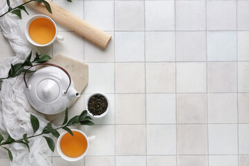 Composition with teapot, cups of tea and bowl with dry leaves on white tile background