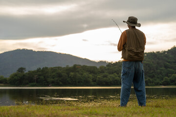 Enjoy moment of Handsome man fishing as a leisure activity during his vacation at the lake on sunset. Silhouette at sunset moment of man fishing rotation with reel.