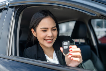 Fototapeta na wymiar Young beautiful asian business women in suit getting new car showing car key. she very happy and excited in hand holding car key. Smiling female driving vehicle on the road city on a bright day