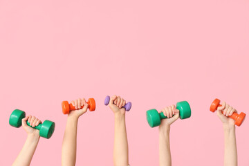 Female hands with different dumbbells on pink background