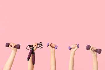 Female hands with dumbbells and skipping rope on pink background