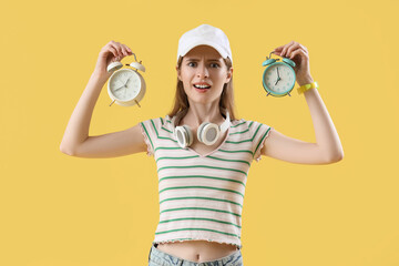 Shocked young woman with alarm clocks on yellow background