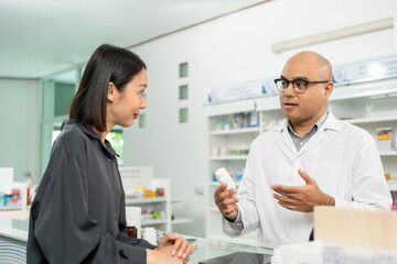 Pharmacist recommends medicines to customers. Asking the questions of medication. Professional Asian male pharmacist giving prescription medications to female patient customers at drugstore shelves.