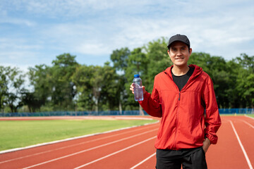 Naklejka premium Handsome indian man drinking water after workout exercising in the stadium. Young asian man drinking water after jogging running outdoor at running track. Healthy and active lifestyle concept.