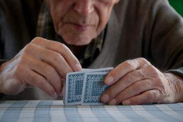 Unrecognized senior man with wrinkled hands holding and playing cards