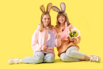 Young girls with Easter bunny ears, flowers and decor on yellow background