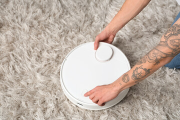 Young man turning on modern robot vacuum cleaner in living room, closeup