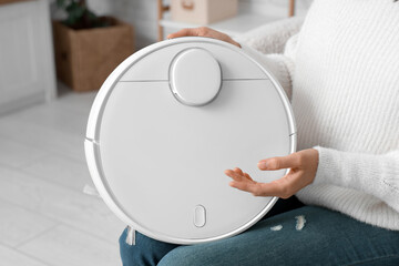 Young woman with modern robot vacuum cleaner in living room, closeup