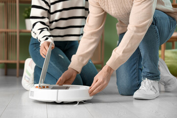 Young couple setting up modern robot vacuum cleaner in living room