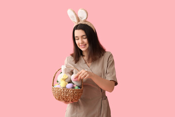 Female massage therapist in bunny ears with Easter eggs and herbal bags on pink background