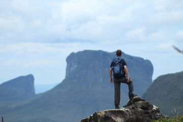 homem de mochila nas costas em trilha na Chapada Diamantina, Bahia, com motanhas ao fundo