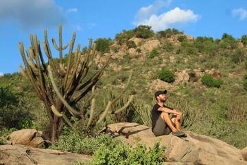 homem sentado em frente a cactos no Serrote do Urubu, em Petrolina, Pernambuco, vegetação da...