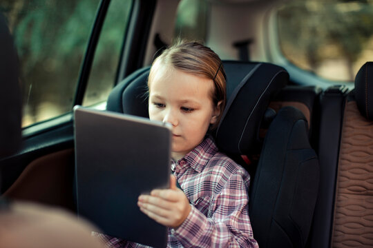 Little girl holding tablet in car backseat