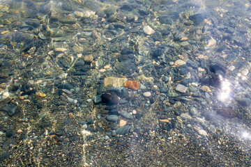Shiny transparent sea water surface with multi colored stones underwater