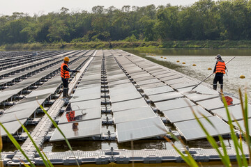 Naklejka premium Worker Cleaning floating solar panels or solar cell Platform system on the lake with brush and water. Worker cleaning solar modules in a Solar Energy Power Plant