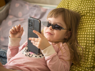 three-year-old girl looking at a smartphone wearing sunglasses