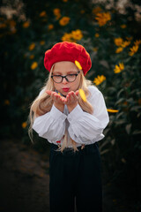 A little blonde girl with glasses and a red beret blows off yellow petals