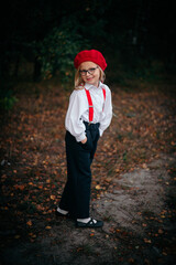 Little blonde girl in glasses, red beret and suspenders in nature