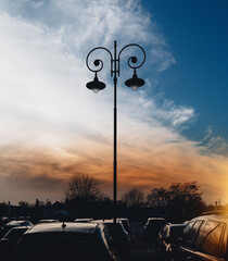 Cars in a parking lot with a city light against the sky at sunset. 