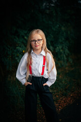 Portrait of a blonde little girl with glasses, a white shirt and red suspenders