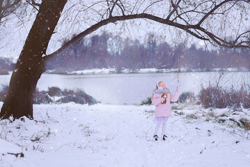 Portrait of a beautiful little girl in winter clothes on the background of a pond