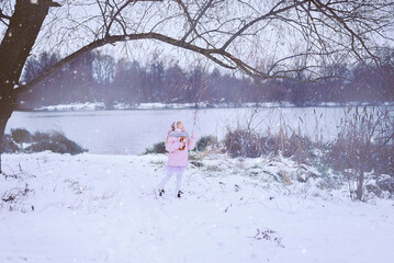 Portrait of a beautiful little girl in winter clothes on the background of a pond