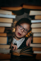 A girl makes faces while reading a book against the background of a stack of books