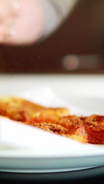 Mujer mayor irreconocible espolvoreando canela sobre torrijas de Semana Santa reci&eacute;n hechas