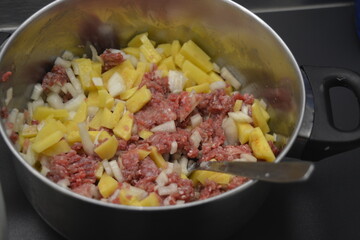 Cooking a delicious and healthy meal, minced meat with onions and sliced potatoes is located in a large metal pot.
