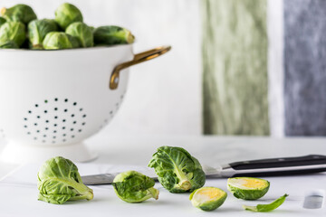 A colander full of raw brussel sprouts with a few on a cutting board in front. - obrazy, fototapety, plakaty