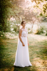 Valmiera, Latvia - July 7, 2023 - A bride in a white wedding dress stands in a sunlit park, looking...
