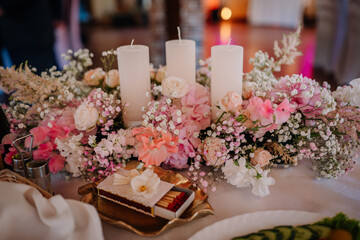 Valmiera, Latvia - July 7, 2023 - A floral wedding centerpiece with pink flowers and white candles...