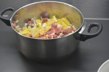 Cooking a delicious and healthy meal, minced meat with onions and sliced potatoes is located in a large metal pot.