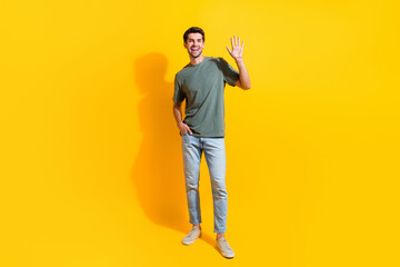 Full length photo of good mood friendly guy wear khaki t-shirt waving arm hi isolated yellow color...