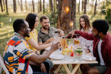 Meeting of multiracial group of friends eating dinner and drinking wine during party in the forest