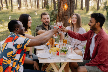 Meeting of multiracial group of friends toasting and drinking wine during party in the forest