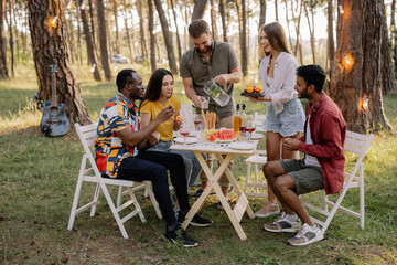 Meeting of multiracial group of friends eating dinner and drinking wine during party in the forest