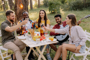 Meeting of multiracial group of friends playing guitar, singing, eating dinner and drinking wine during party in the forest