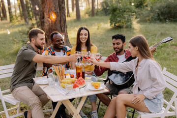 Meeting of multiracial group of friends playing guitar, singing, eating dinner and drinking wine during party in the forest