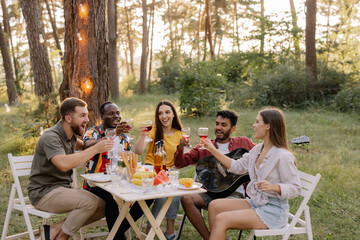 Meeting of multiracial group of friends playing guitar, singing, eating dinner and drinking wine during party in the forest