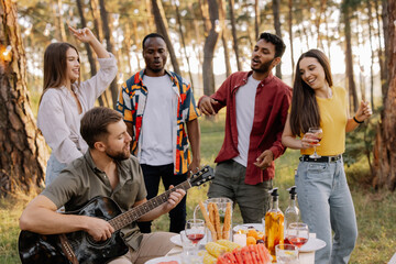 Multicultural group of people, bearded hipster man playing guitar and friends dancing and having fun