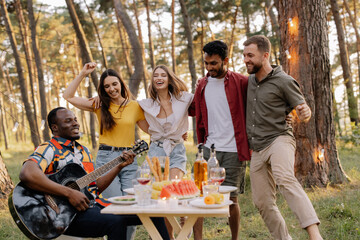 Multicultural group of people, African hipster man playing guitar and friends dancing, singing and having fun