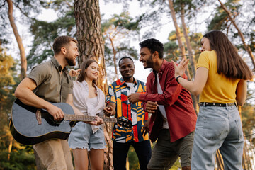 Multiracial group of people, bearded hipster man playing guitar and friends dancing, singing and having fun