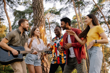 Multiracial group of people, bearded hipster man playing guitar and friends dancing, singing and having fun