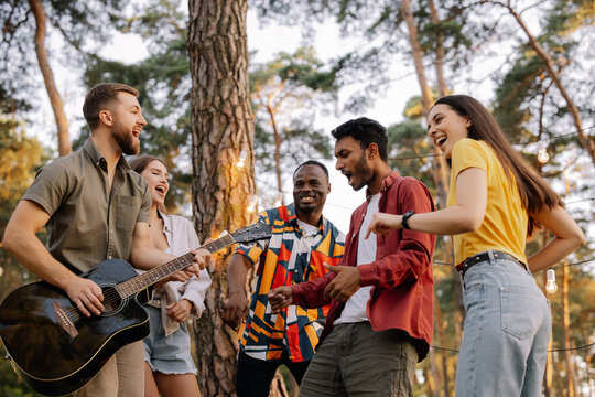 Multiracial group of people, bearded hipster man playing guitar and friends dancing, singing and having fun