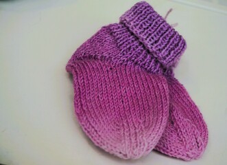 Lilapinke selbstgestrickte Babysocken aus Wolle auf weißer Tischfläche 