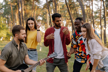 Multiracial group of people, bearded hipster man playing guitar and friends dancing, singing and having fun
