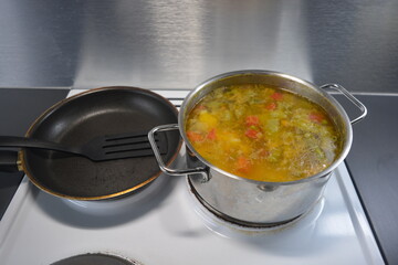 Cooking delicious and healthy food, hot fresh soup from vegetables and meat. The hot dish is cooked in a metal pot and placed on a white kitchen stove.
